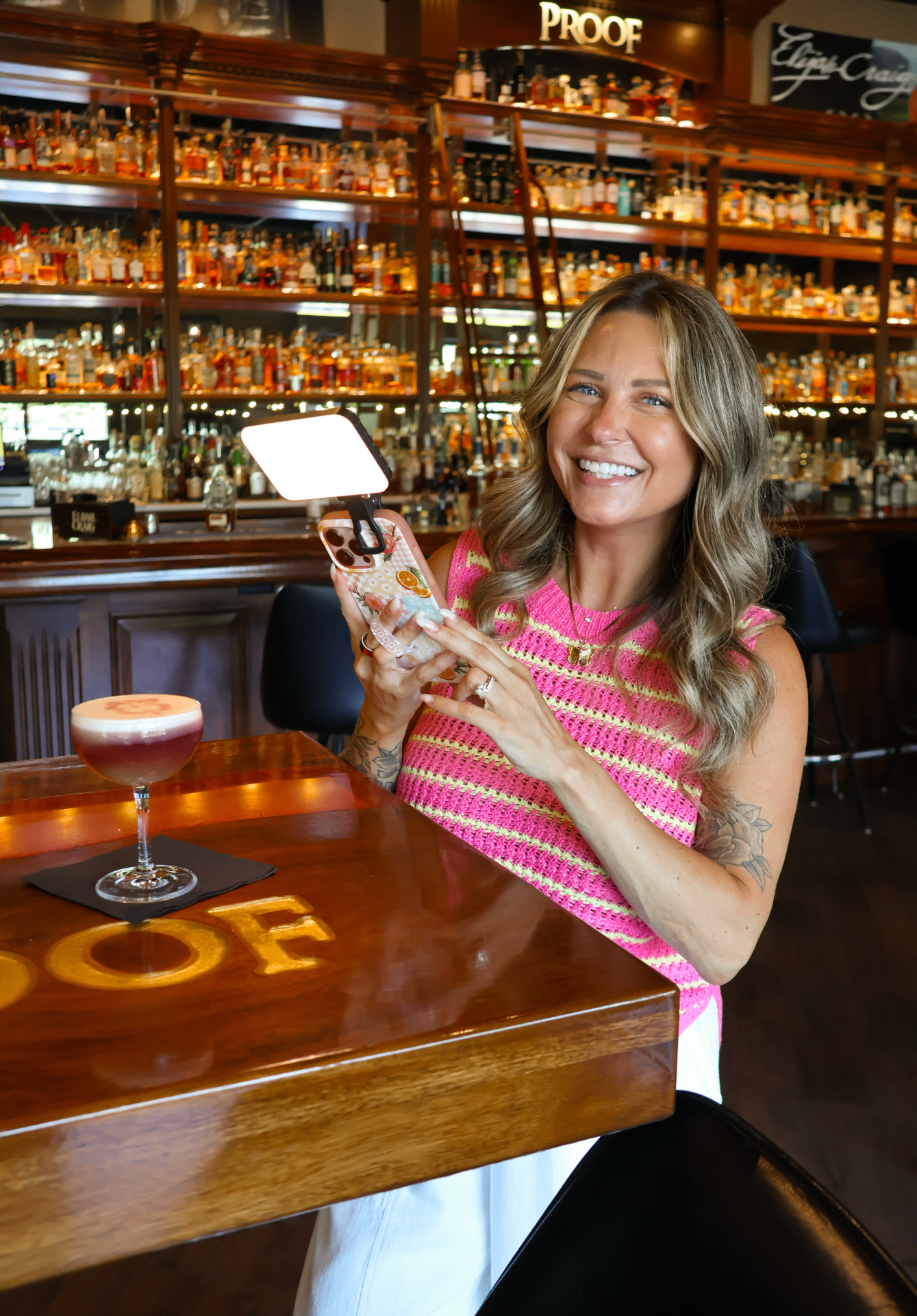 Honey Edit founder capturing content at a bourbon bar with a phone-mounted light and craft cocktail